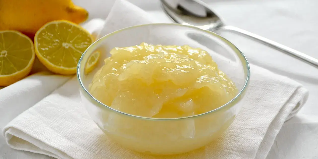 Una ciotola di deliziosa crema al limone senza uova, con limoni freschi affettati sullo sfondo.