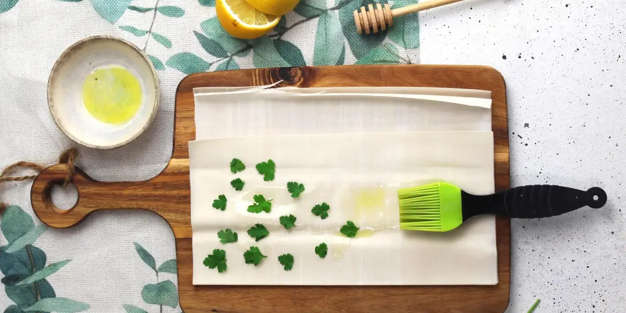 Preparazione per un piatto con pasta fillo: ingredienti come limone, miele, prezzemolo e olio su un tagliere.