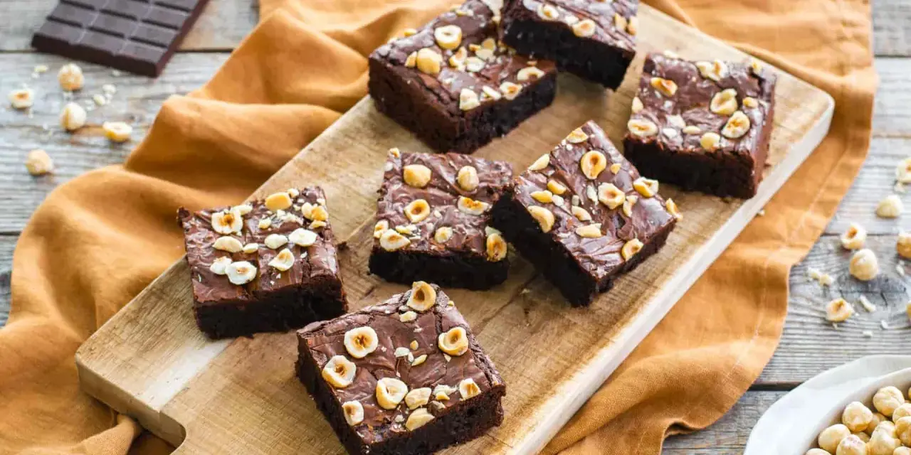 Deliziosi brownie senza glutine con nocciole tostate su tagliere di legno.