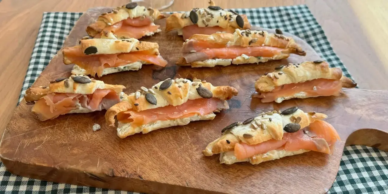 Cornetti di pasta sfoglia ripieni di salmone affumicato e formaggio cremoso, guarniti con semi.