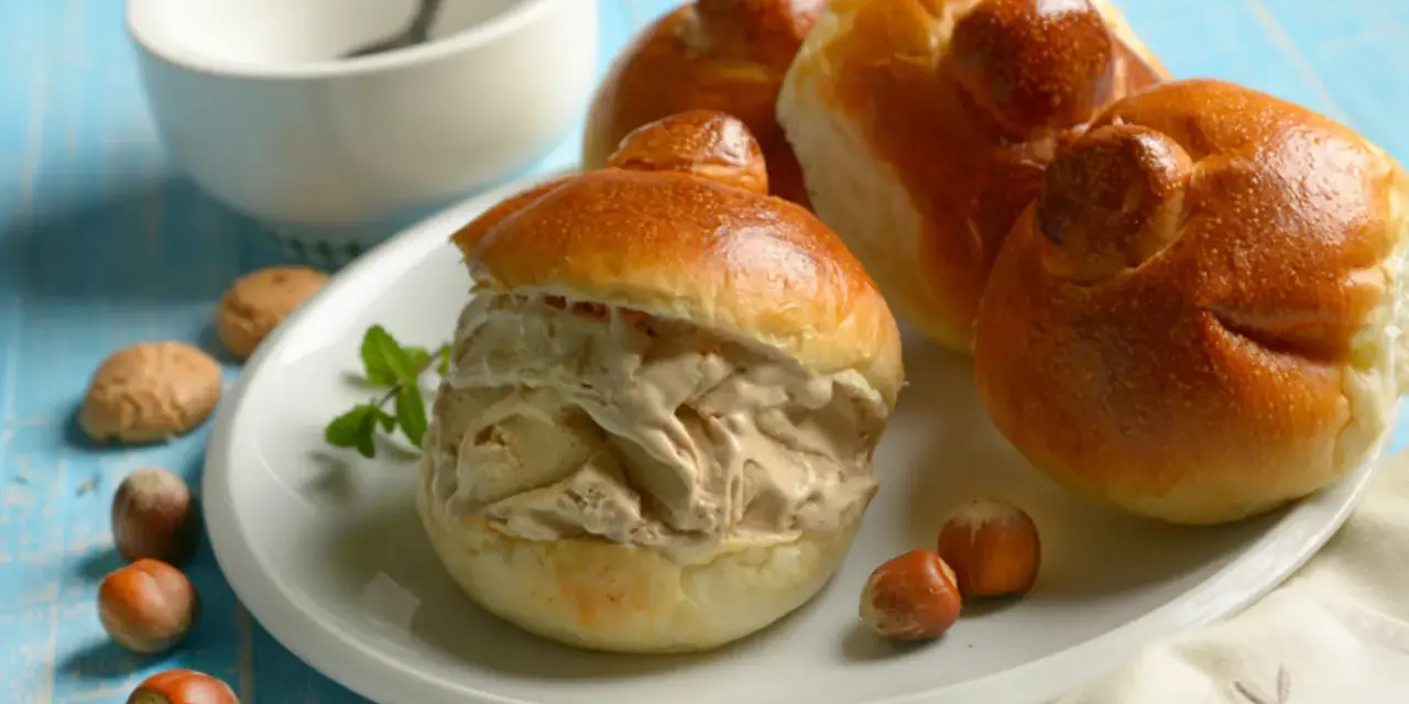 Brioches col tuppo, soffici e dorate, ripiene di gelato cremoso. Un dolce siciliano da gustare con nocciole e menta.