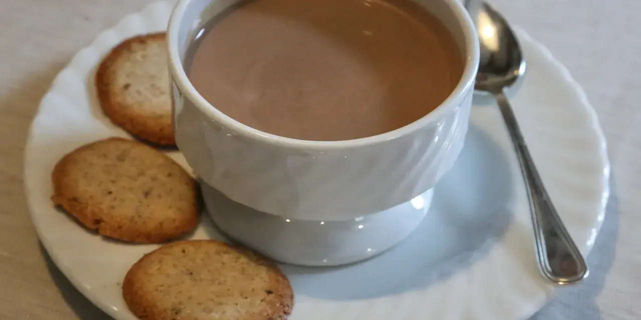 Tazza di crema di cogne fumante con biscotti secchi su un piattino bianco, accompagnata da un cucchiaino.
