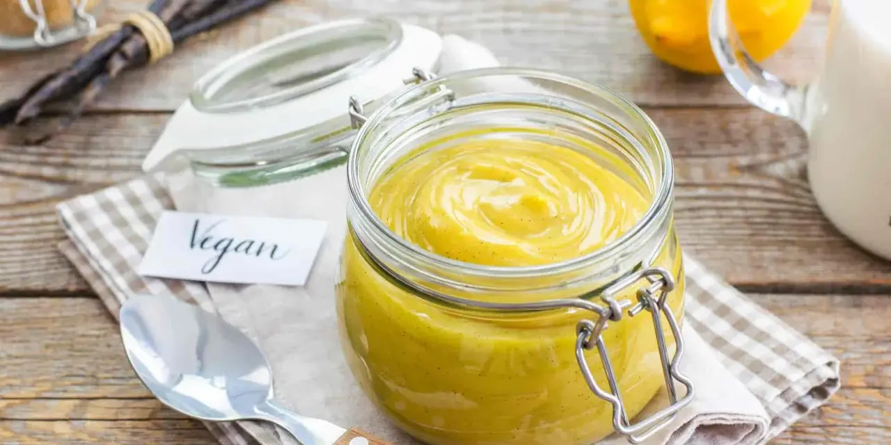 Crema pasticcera vegana in un barattolo di vetro, con bacche di vaniglia e limoni sullo sfondo.