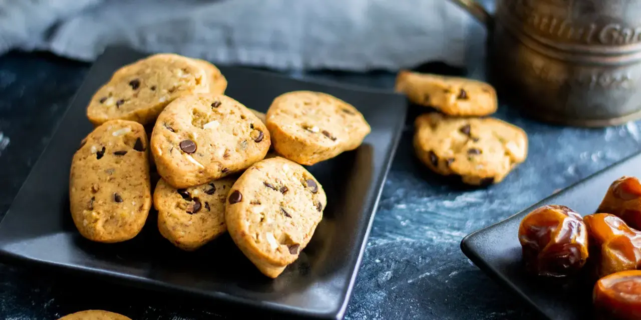 Biscotti vegan con gocce di cioccolato e datteri su piatti neri, pronti per una pausa golosa.