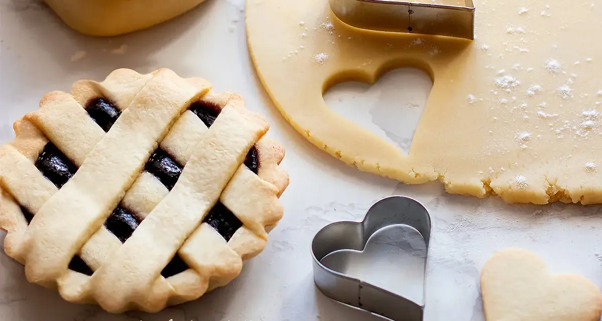 Una crostata con ripieno di marmellata, pasta frolla stesa e tagliabiscotti a forma di cuore.