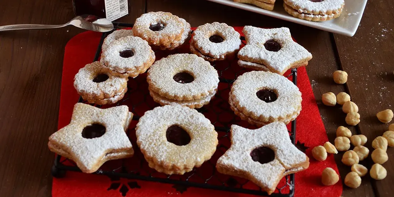 Deliziosi biscotti Linzer, a forma di stella e tondi, ripieni di marmellata e spolverati di zucchero a velo, su una griglia nera.