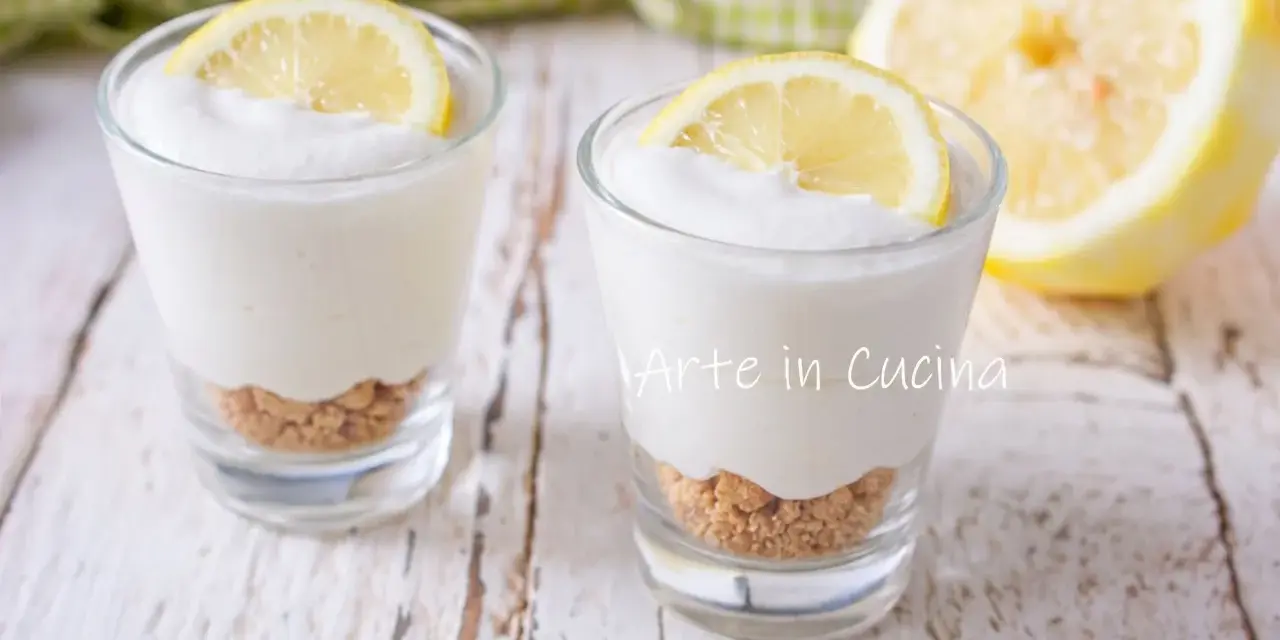 Due bicchierini di mousse al limone con base croccante e fetta di limone, su un tavolo di legno.