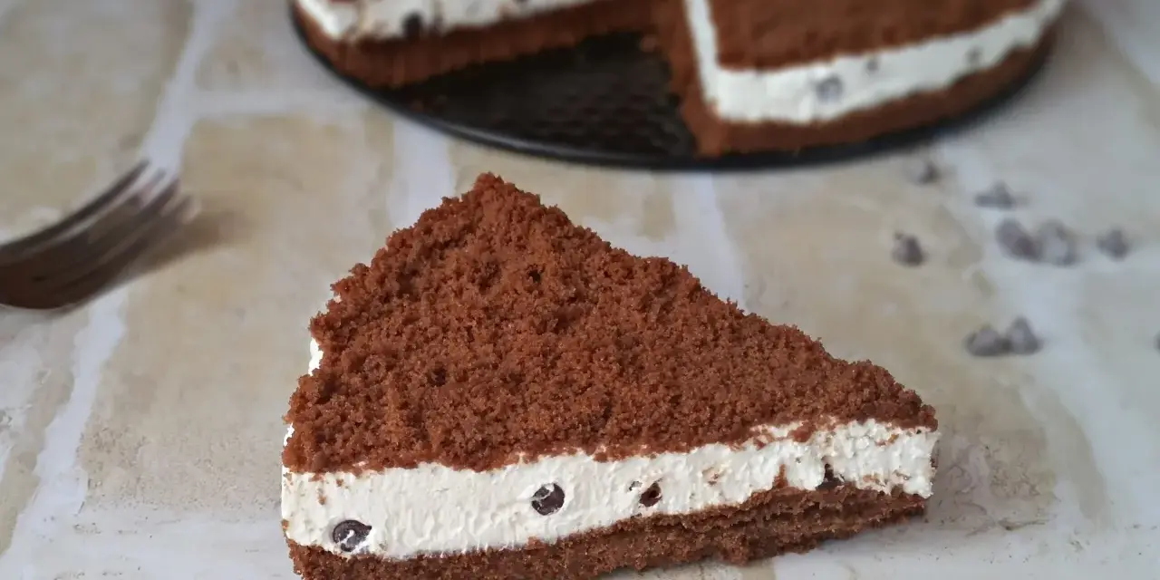 Una fetta di torta al cioccolato con ripieno cremoso al mascarpone e biscotti sbriciolati, decorata con gocce di cioccolato.