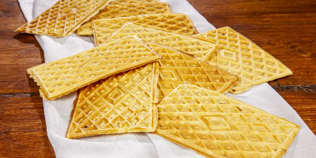 Un mucchio di croccanti ferratelle abruzzesi, dolci tradizionali, disposte su un panno bianco su un tavolo di legno.