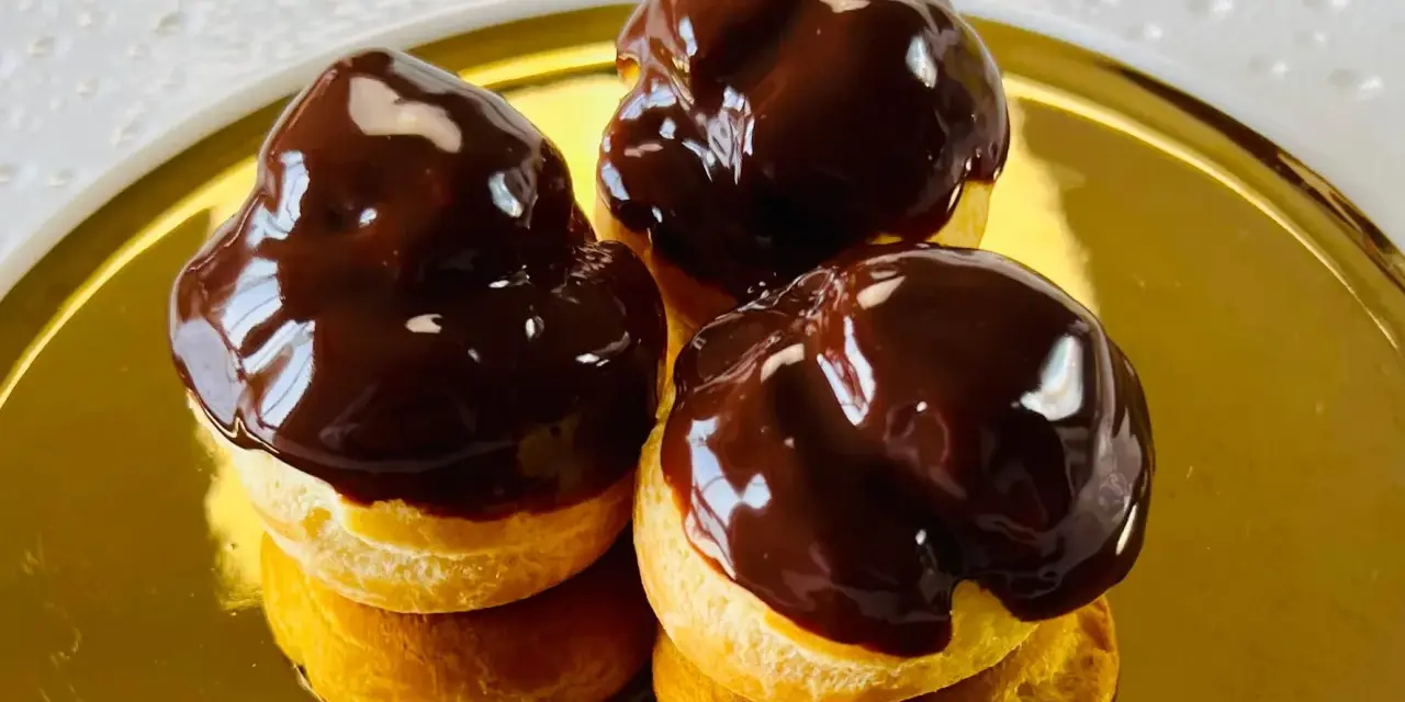 Tre golosi bignè al cioccolato, lucidi e invitanti, su un piatto dorato.