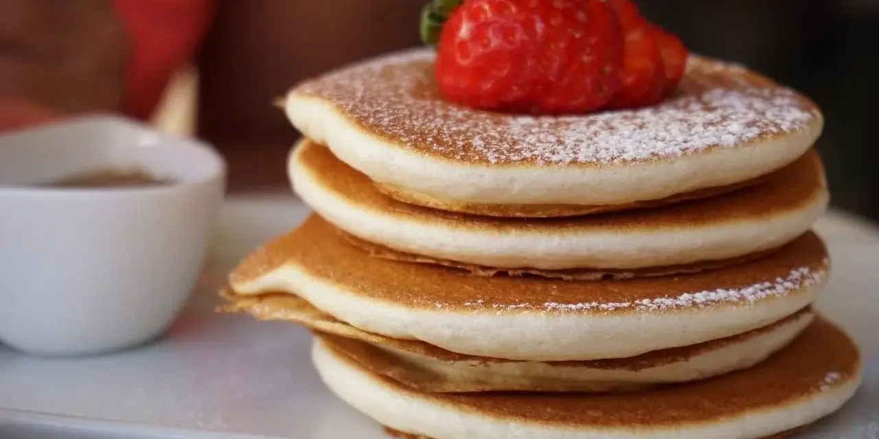 Pancake Bimby perfetti, impilati e spolverati di zucchero a velo, con una fragola fresca in cima.