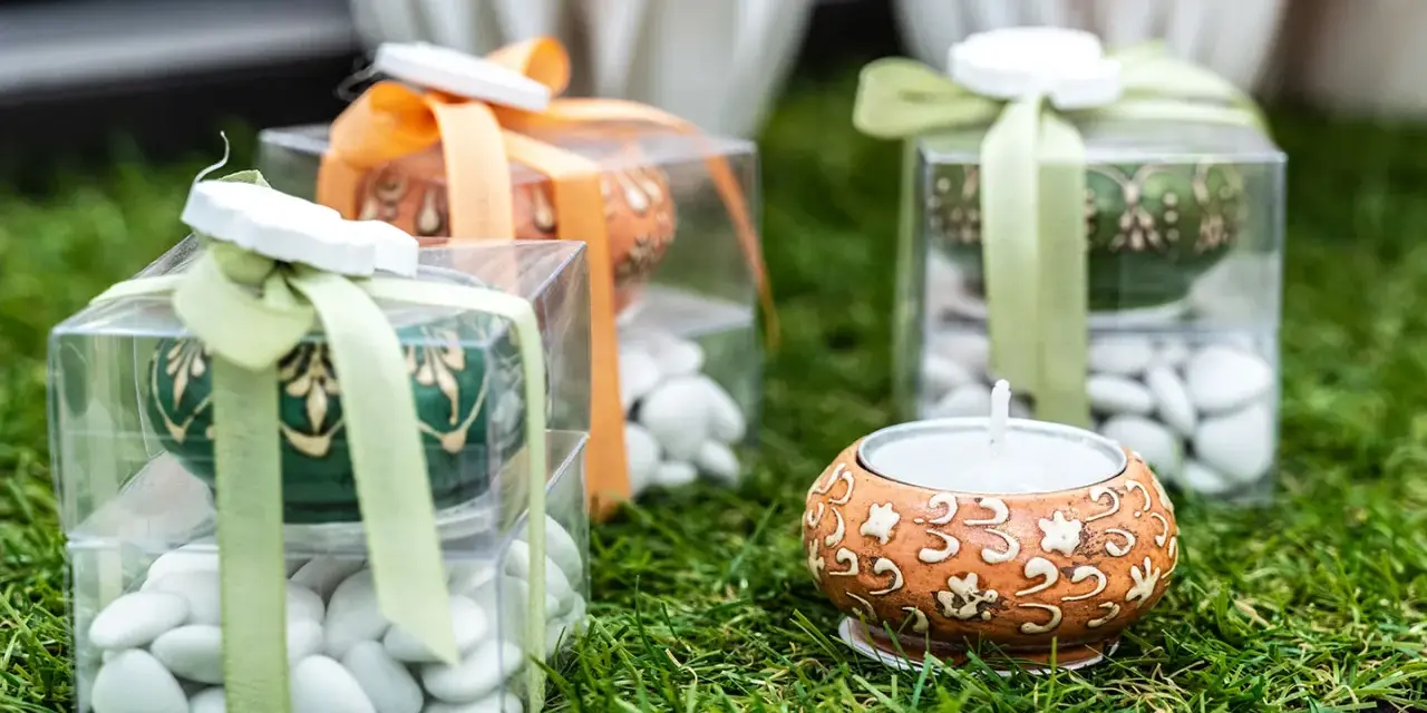 Confezioni regalo con confetti bianchi, candela e decorazioni floreali. Il significato dei confetti, augurio di dolcezza e prosperità.
