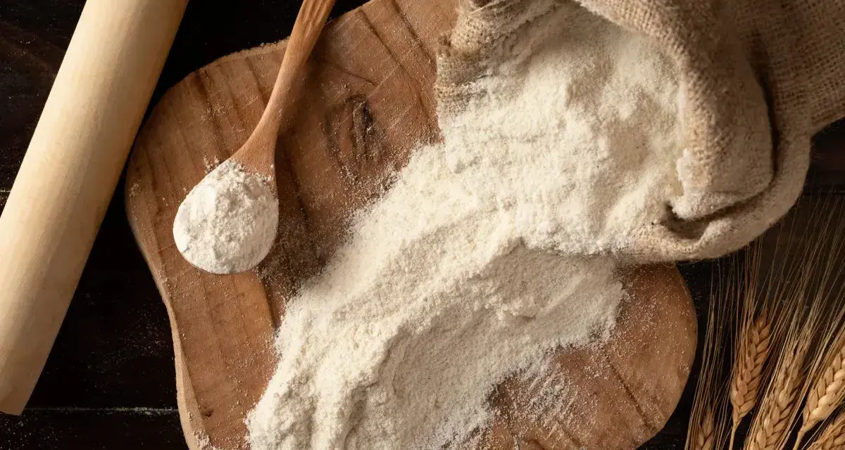 Farina 0 al posto della 00 nei dolci: un sacco di farina, un mestolo e spighe di grano su un tagliere di legno.