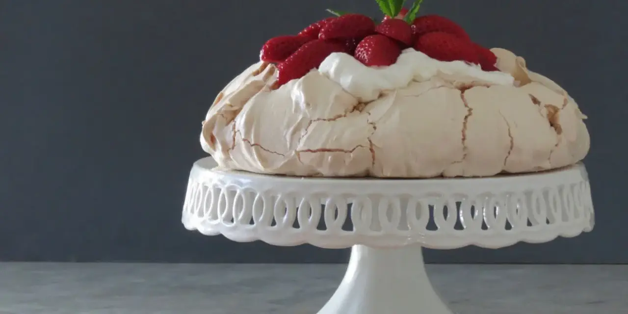 Pavlova ricetta: meringa croccante fuori e morbida dentro, guarnita con panna montata e fragole fresche.