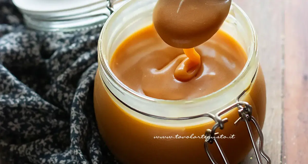 Un cucchiaio raccoglie un denso caramello salato senza panna da un barattolo di vetro.