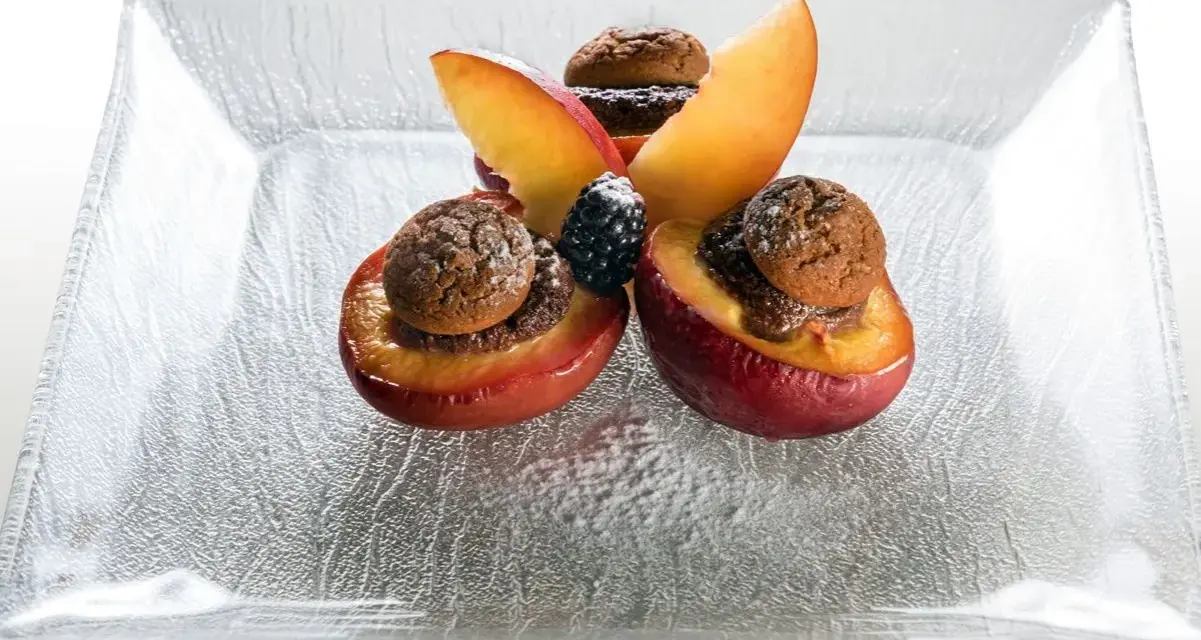 Deliziose pesche ripiene con biscotti e frutti di bosco, un dolce invitante su un piatto di vetro.