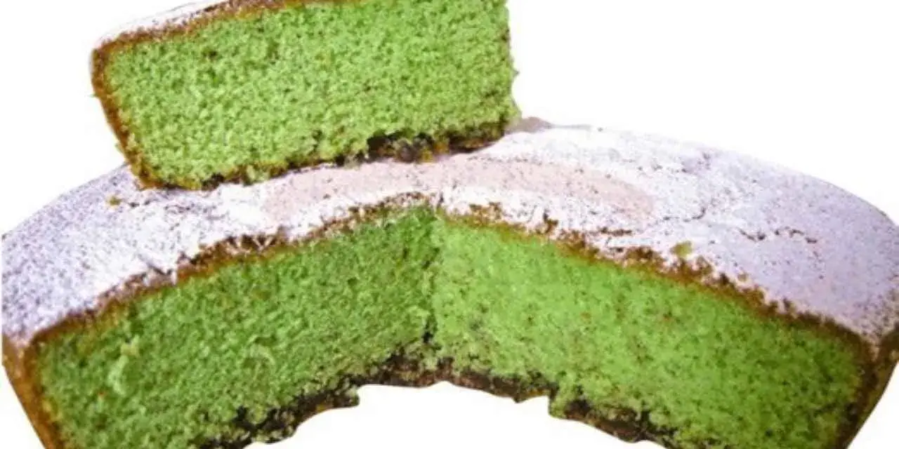 Una fetta di torta alla menta verde brillante, cosparsa di zucchero a velo, è appoggiata su una torta intera.