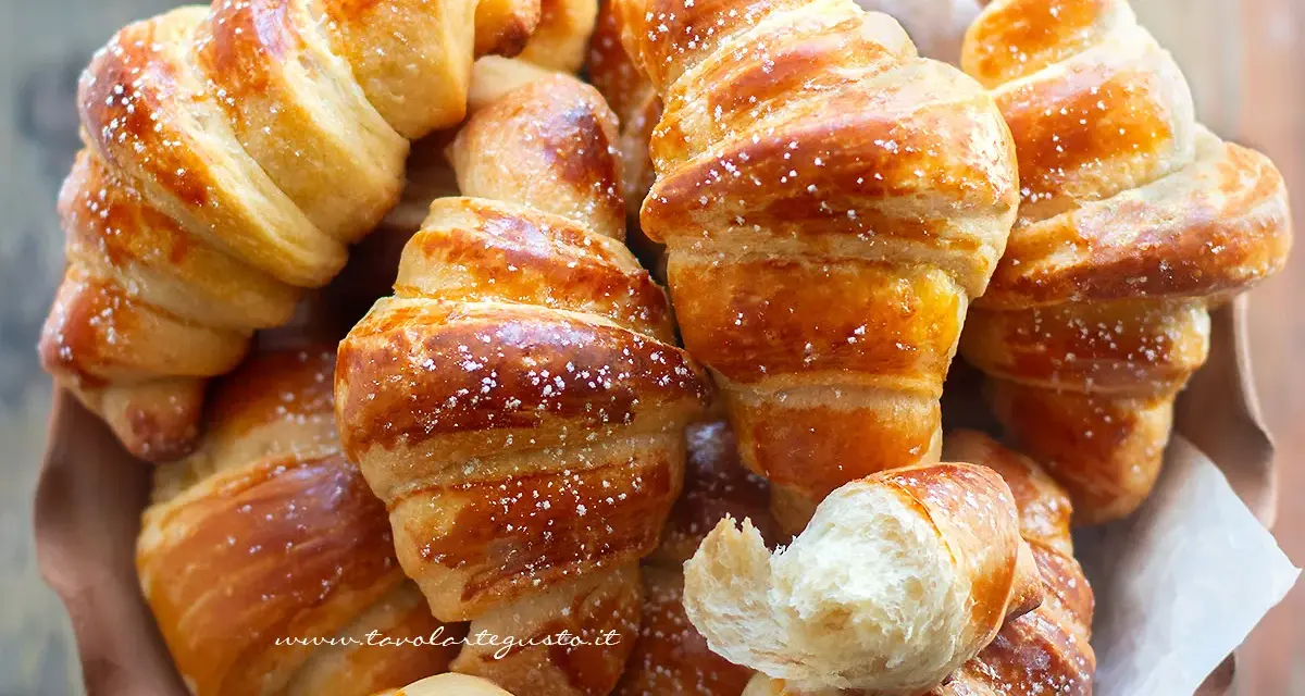 Brioches fatte in casa, dorate e soffici, cosparse di zucchero a velo. Un profumo invitante che ricorda la colazione perfetta.