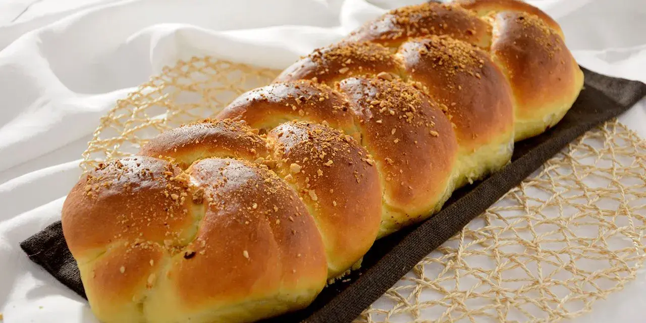 Treccia dorata di dolci con farina manitoba, cosparsa di granella croccante, su un letto di lino bianco.