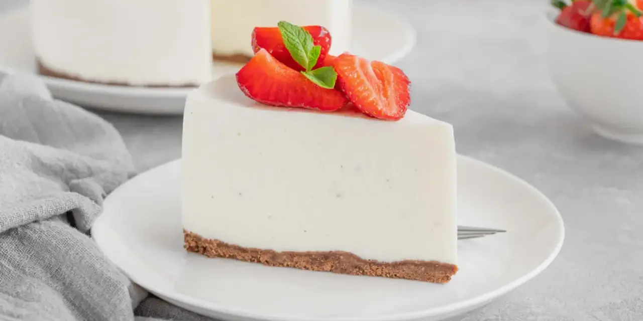 Una fetta di torta fredda allo yogurt senza biscotti, guarnita con fragole fresche e menta, su un piatto bianco.