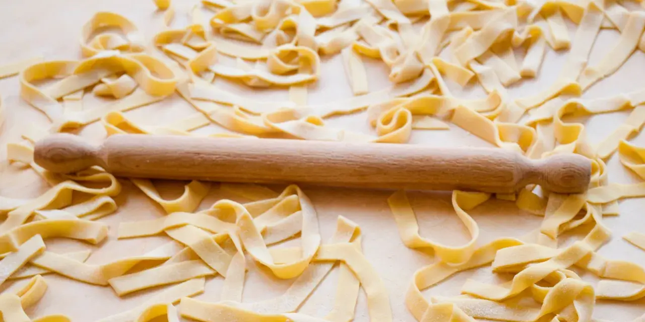 Fettuccine fresche sparse su un piano di lavoro, con un mattarello in legno. La farina, che è all-purpose flour, è visibile sulla pasta.