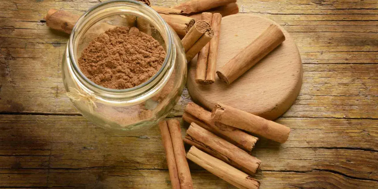 Barattolo di cannella in polvere e bastoncini su un tagliere di legno. Ingredienti essenziali per la cucina.