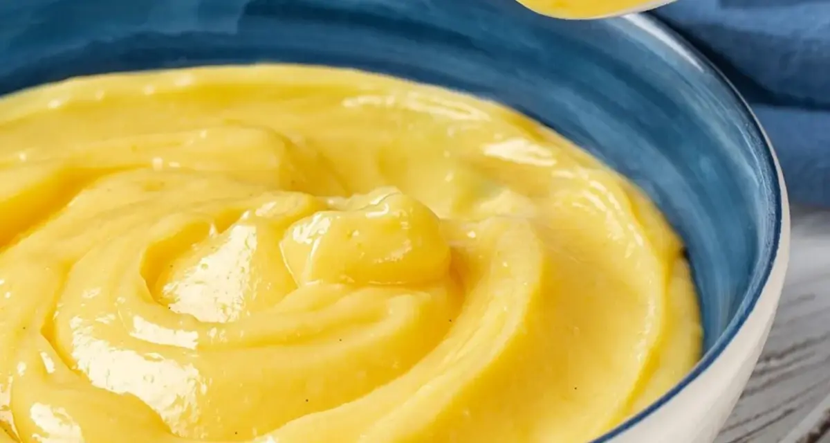 Una ciotola blu piena di deliziosa crema pasticcera senza uova, con un cucchiaio che ne preleva una porzione.