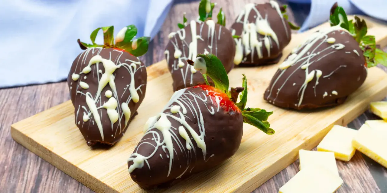 Fragole ricoperte di cioccolato fondente e decorate con cioccolato bianco. Un delizioso assaggio di frutta al cioccolato su un tagliere di legno.