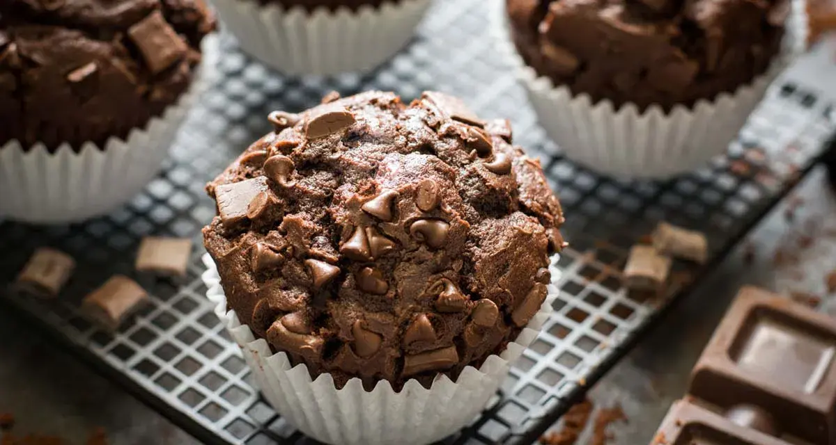Muffin al cioccolato ricchi e golosi, con gocce e pezzi di cioccolato fondente, su una griglia con cacao e tavolette di cioccolato.