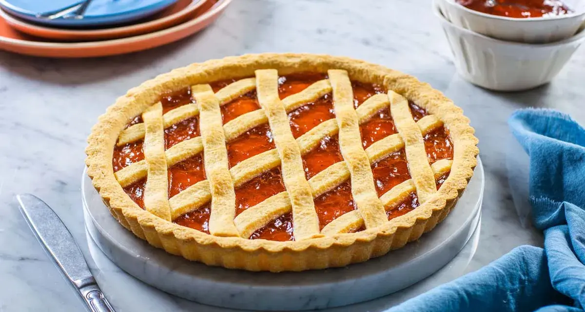 Crostata alla marmellata dorata, perfetta per il tempo cottura crostata forno statico. Servita su un piatto di marmo con tovagliolo blu.