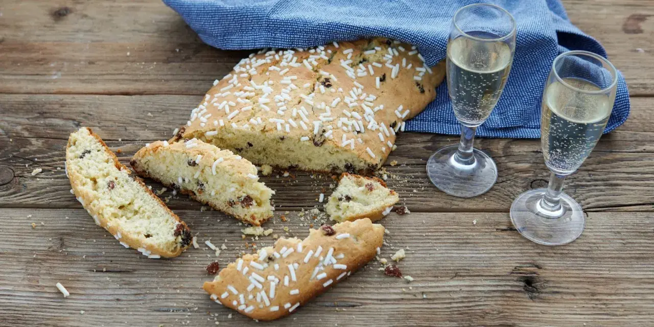 Fette di ciambella romagnola, cosparse di zuccherini, accanto a due bicchieri di spumante.
