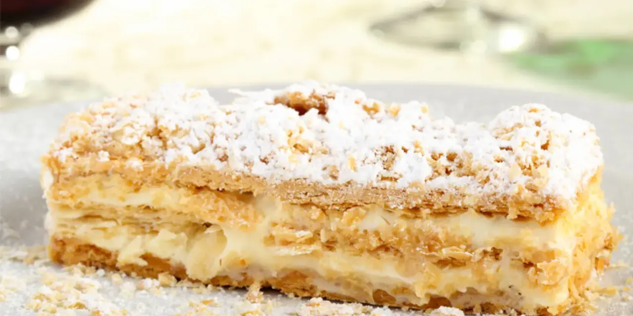 Una fetta di rettangolare torta millefoglie compleanno, con crema pasticcera e zucchero a velo.