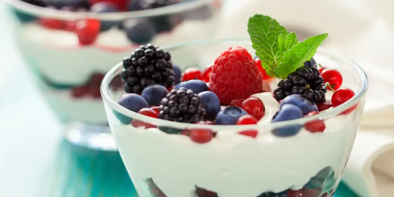 Deliziosa mousse allo yogurt con frutti di bosco freschi e una fogliolina di menta, servita in coppette di vetro.