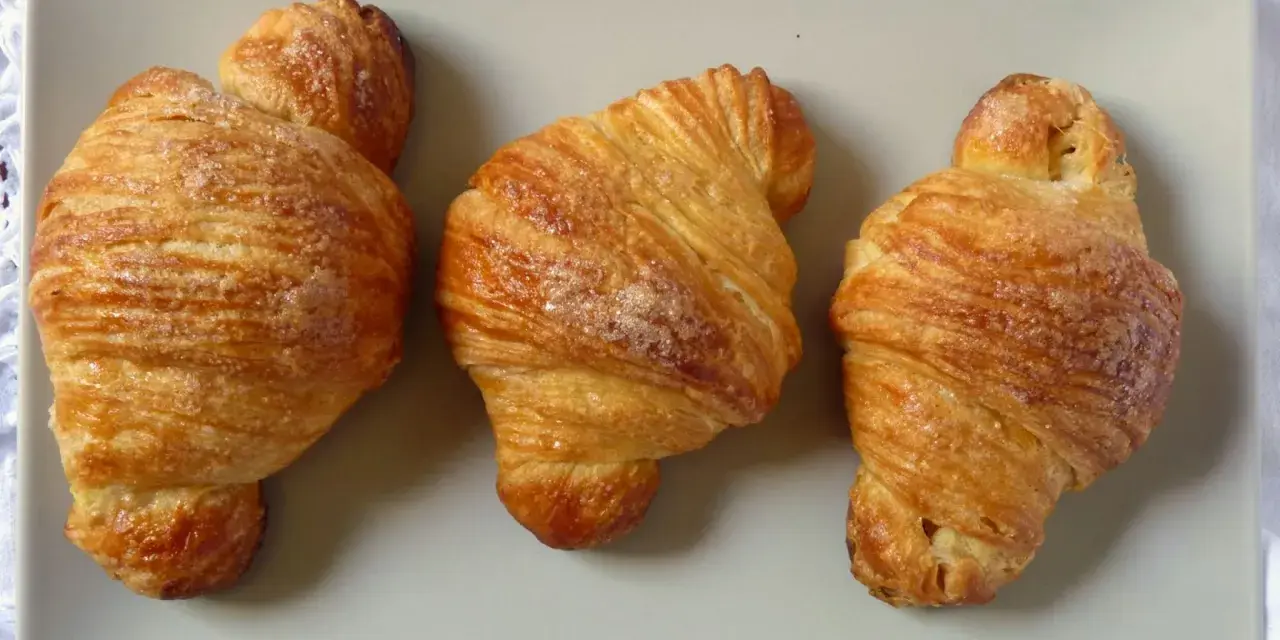 Tre deliziosi croissant dorati, cosparsi di zucchero, disposti su un piatto grigio.