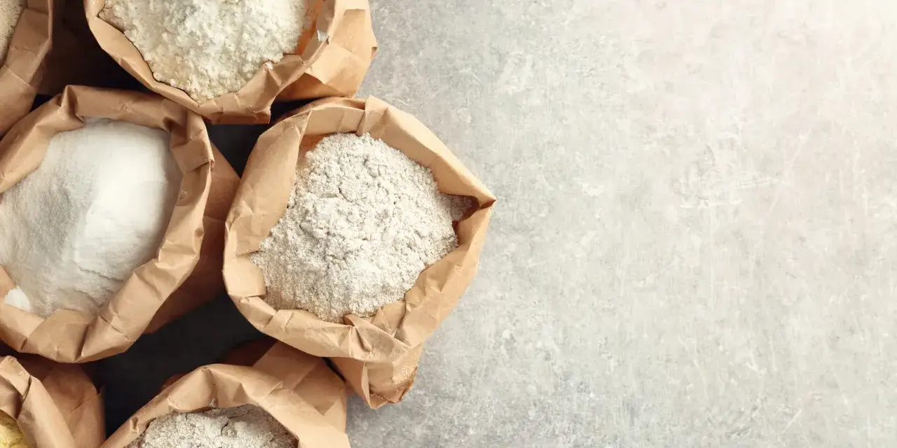 Sacchetti di carta aperti pieni di diverse farine, tra cui farina 0 e manitoba, pronte per creare pane e dolci.