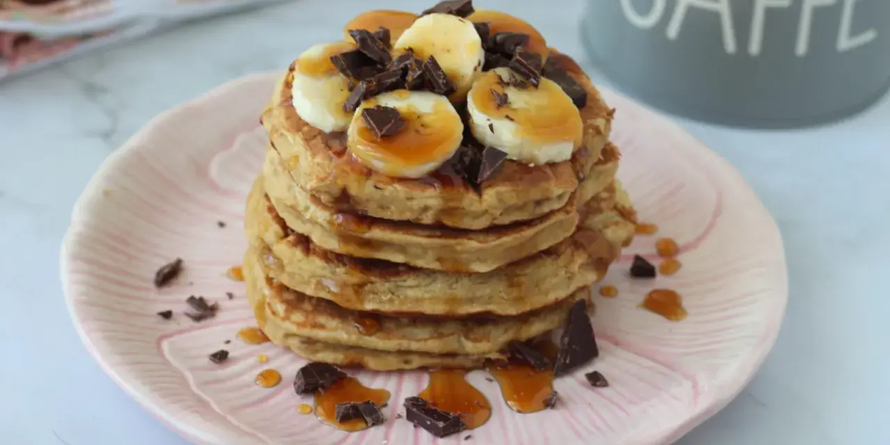 Pancake light con banana, cioccolato e sciroppo d'acero su un piatto rosa.