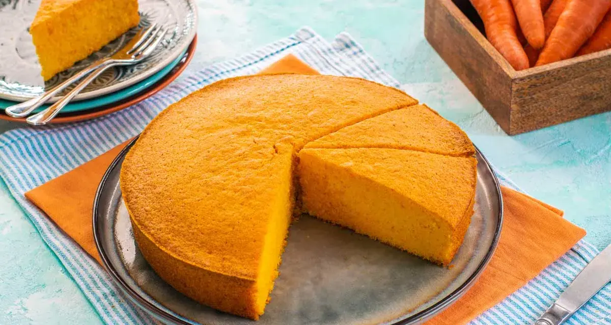Una deliziosa torta di carote, appena sfornata, è tagliata a fette su un piatto. Accanto, un cesto di carote fresche.