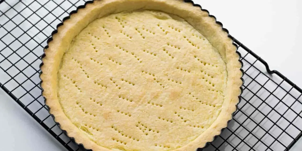 Base di pasta frolla appena sfornata, con fori per la cottura, su una griglia metallica.