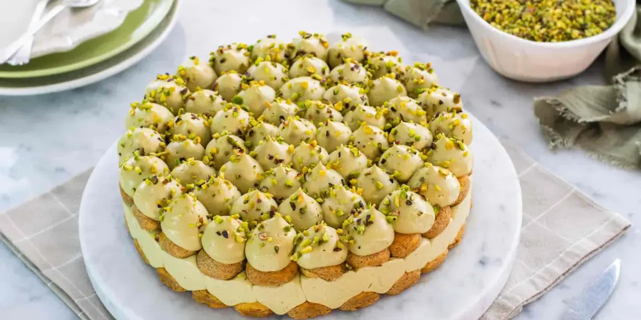 Torta rotonda con tante piccole meringhe verdi, guarnite con granella di pistacchio. Un delizioso tiramisù al pistacchio pronto per essere gustato.