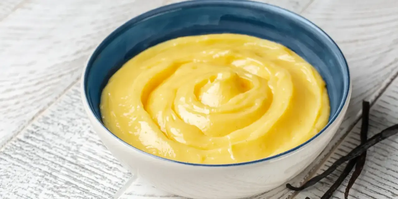 Una ciotola di crema gialla, liscia e invitante, con baccelli di vaniglia accanto. Perfetta per ogni ricetta crema.