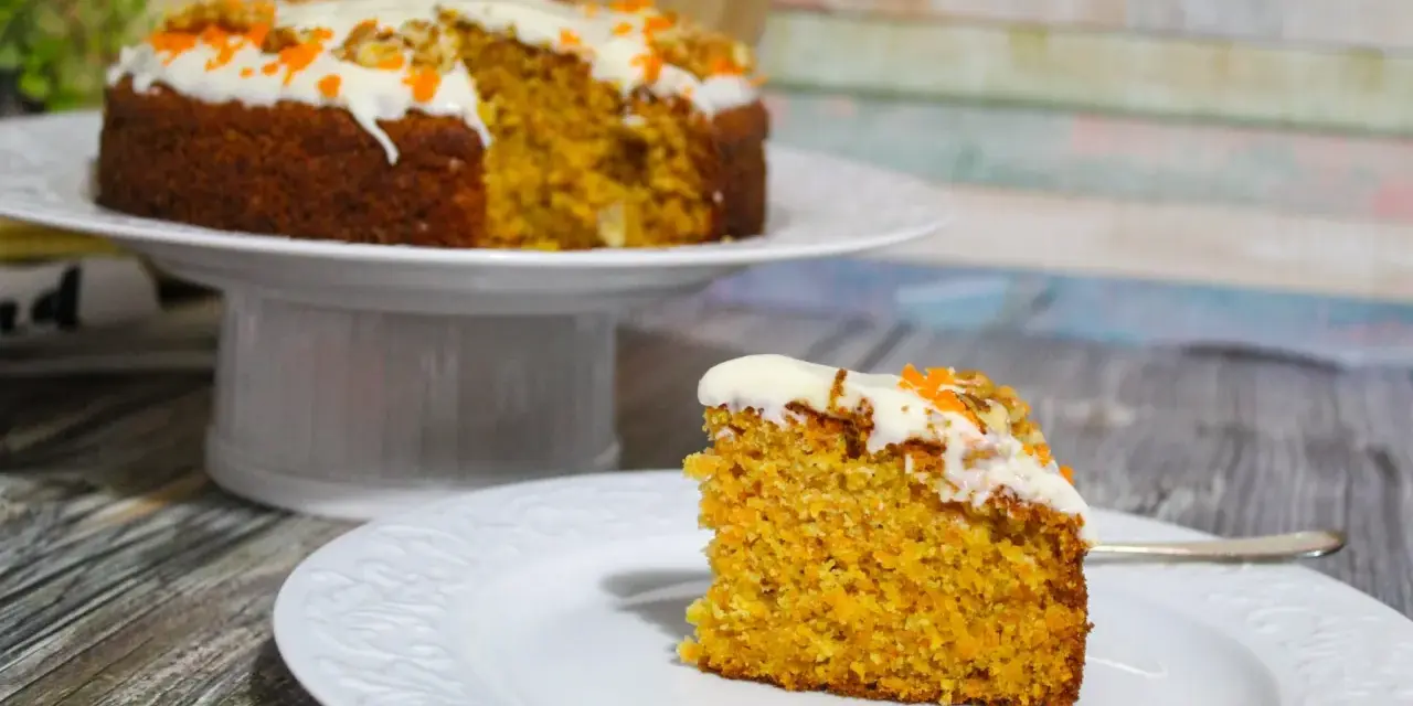 Una fetta di torta di carote senza glutine, soffice e profumata, con glassa bianca e decorazioni arancioni.