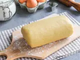 Rotolo di pasta frolla con strutto, pronto per essere trasformato in deliziosi biscotti. Ingredienti base visibili: farina, uova.