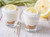 Due bicchierini di mousse al limone con base croccante e fetta di limone, su un tavolo di legno.