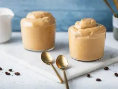 Due bicchieri di soffice crema di caffè, perfetta ricetta crema di caffè senza panna e senza caffè solubile. Due cucchiaini dorati e chicchi di caffè completano la scena.