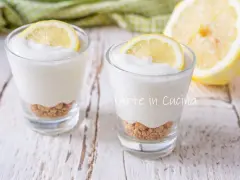 Due bicchierini di mousse al limone con base croccante e fetta di limone, su un tavolo di legno.