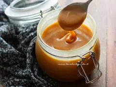 Un cucchiaio raccoglie un denso caramello salato senza panna da un barattolo di vetro.