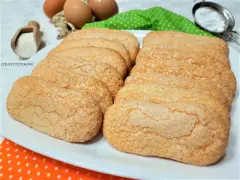 Savoiardi fatti in casa dorati e friabili, pronti per il tiramisù. Ingredienti freschi sullo sfondo.