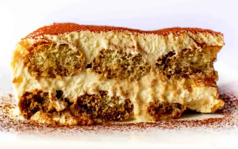 Una fetta di tiramisù, con strati di savoiardi inzuppati e crema al mascarpone, spolverata di cacao. La ricetta perfetta per un dolce indimenticabile.