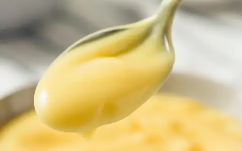 Crema pasticcera lucida su un cucchiaio. Il burro la rende vellutata e lucida, perfetta per farcire dolci.