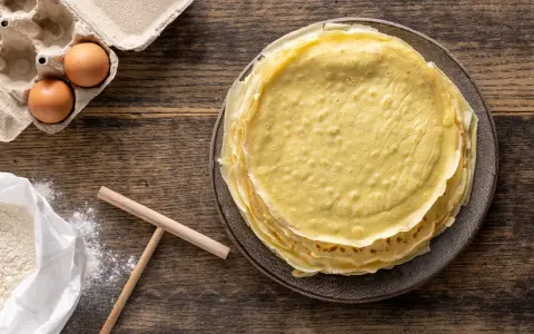 Pila di crepes dorate, pronte per essere farcite. Accanto, uova fresche e farina, ingredienti perfetti per crepes 2 uova.